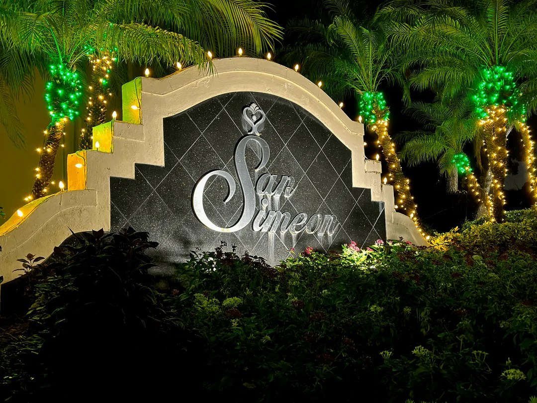 San Simeon community entrance sign framed by palm trees in holiday lighting