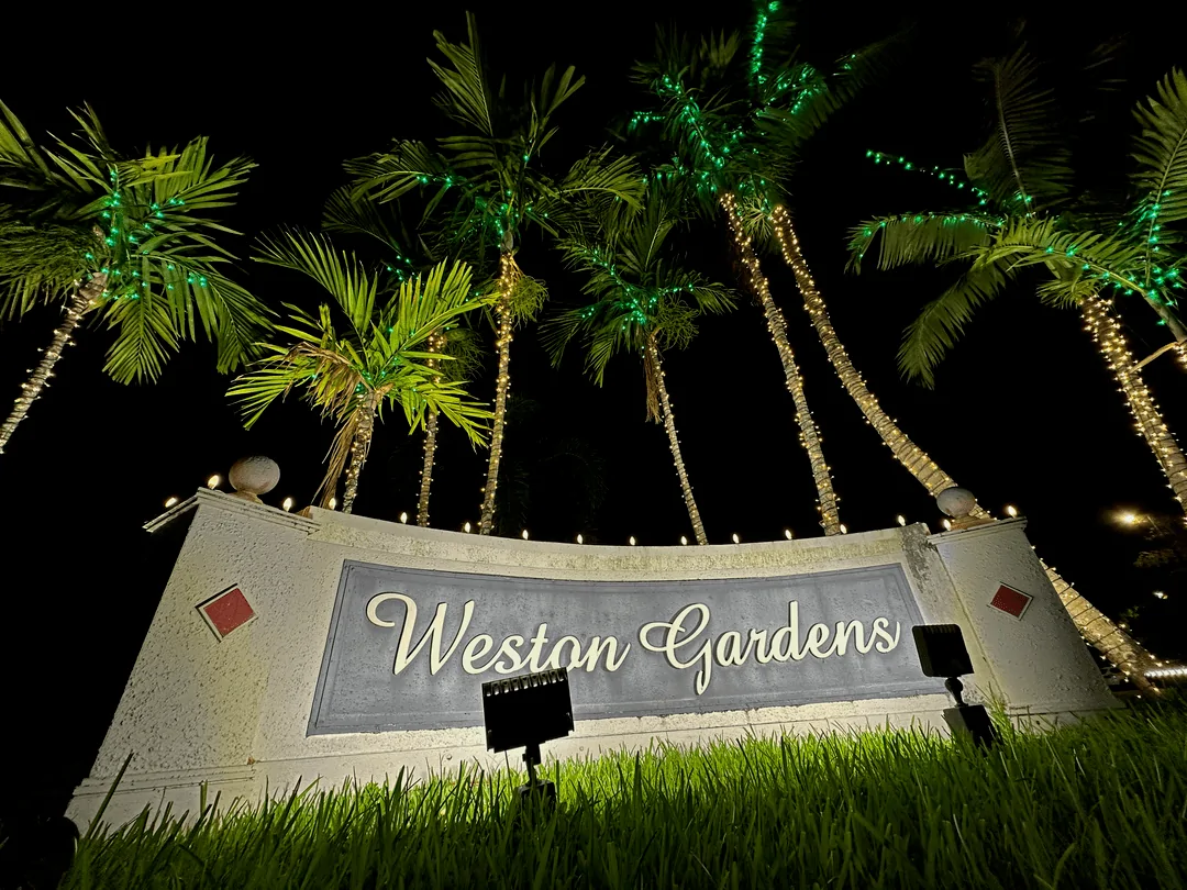 Weston Gardens monument sign with uplit palm trees