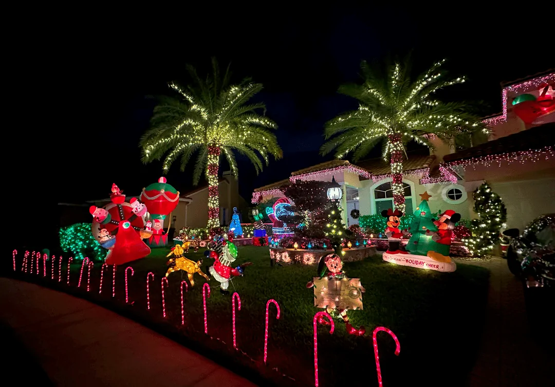 Festive home with candy-cane path lights, inflatable characters, and lit palms