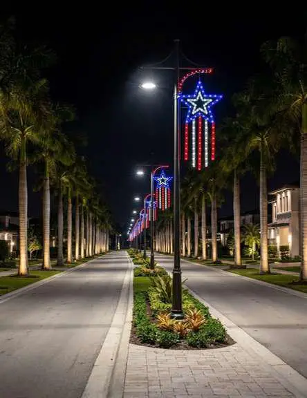 Community boulevard lined with illuminated red, white, and blue star and stars-and-stripes light displays on lampposts at night